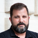 A photo of Richard from the shoulders up while he is standing outside of a building and wearing a black polo shirt.